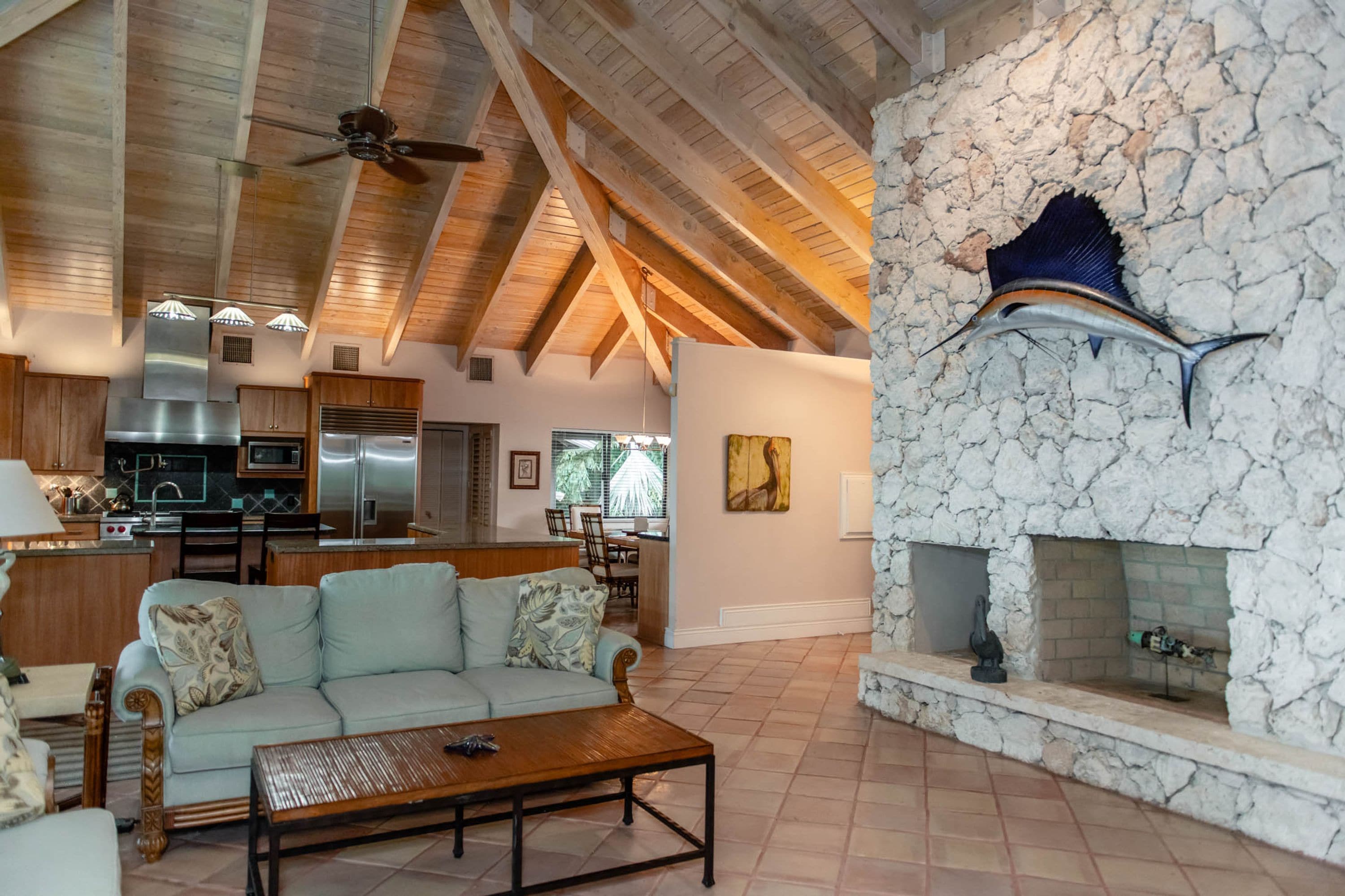 A spacious living area with a high ceiling, a stone fireplace, and a modern kitchen in the background.