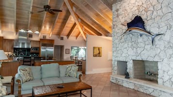 A spacious living area with a high ceiling, a stone fireplace, and a modern kitchen in the background.