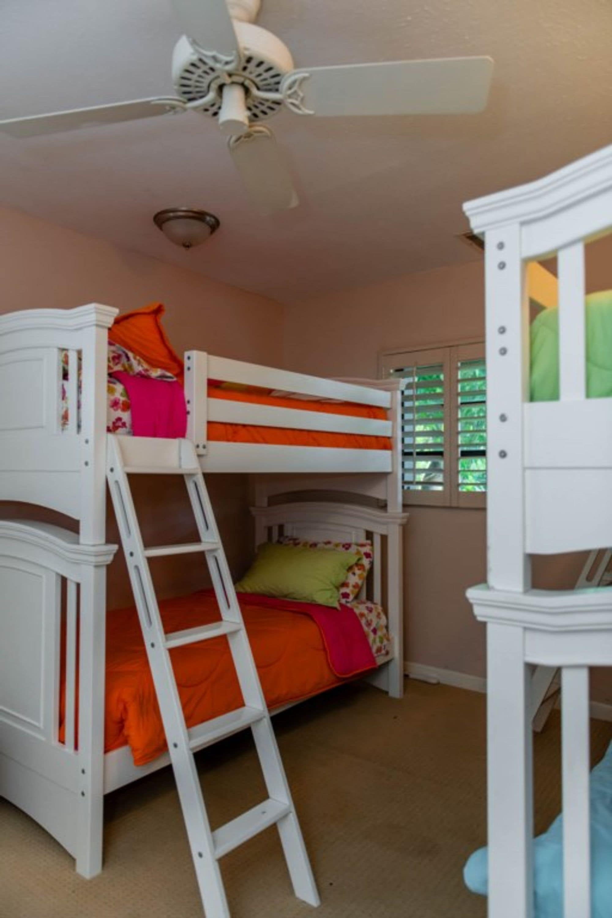 A bunk bed with a ladder, a ceiling fan, and a window with blinds.