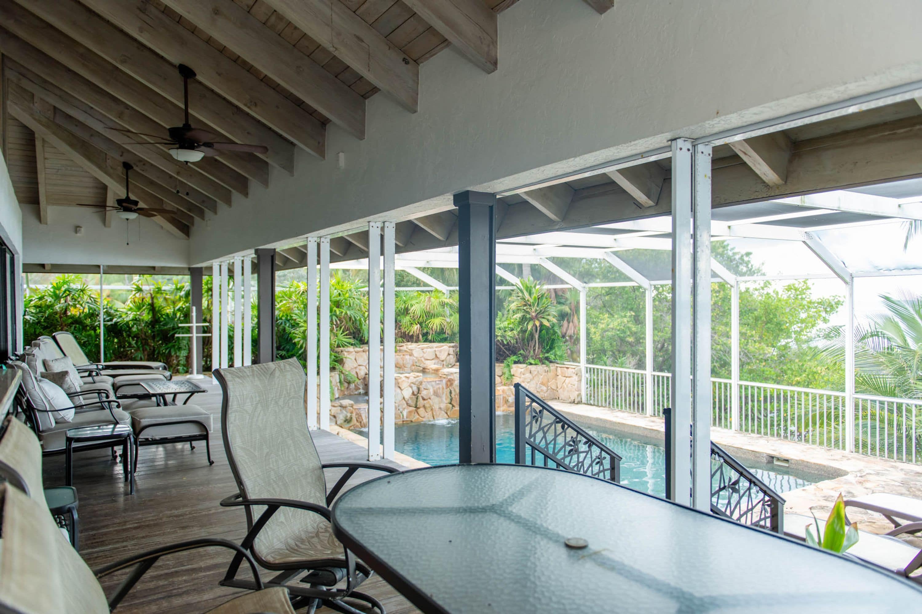 A covered outdoor area with a pool, lounge chairs, and a table.