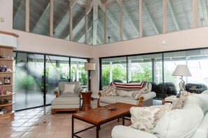 A spacious living room with a high ceiling, large windows, and a view of greenery outside. - Coral Sunset in Islamorada (Tavernier)