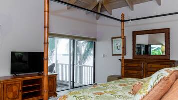 A bedroom with a four-poster bed, a television on a wooden cabinet, a large mirror, and a sliding glass door leading to a balcony.