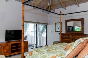A bedroom with a four-poster bed, a television on a wooden cabinet, a large mirror, and a sliding glass door leading to a balcony. - Coral Sunset in Islamorada (Tavernier)