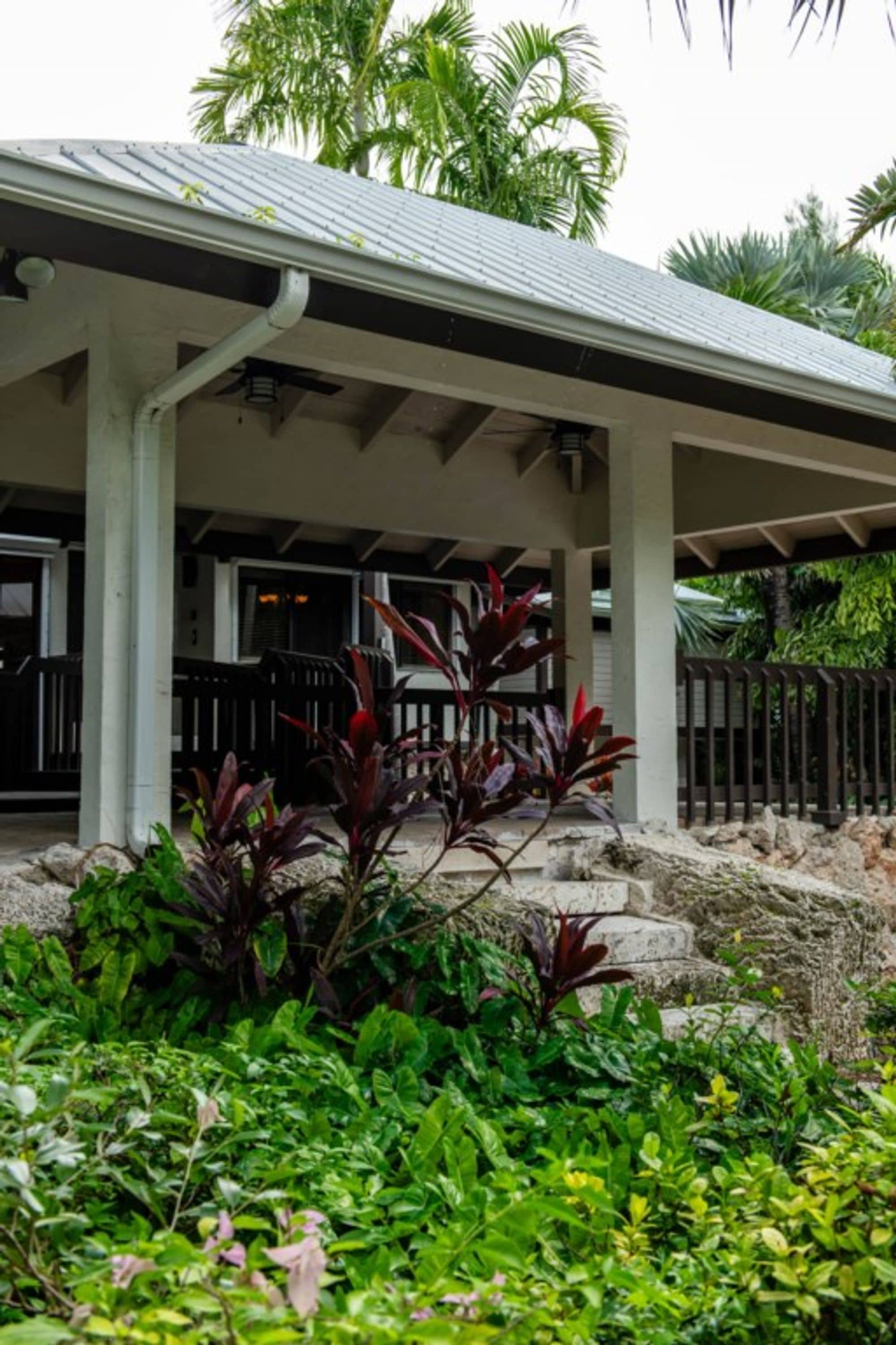 A covered outdoor area with a metal roof, concrete columns, and a stone pathway leading to a building entrance.