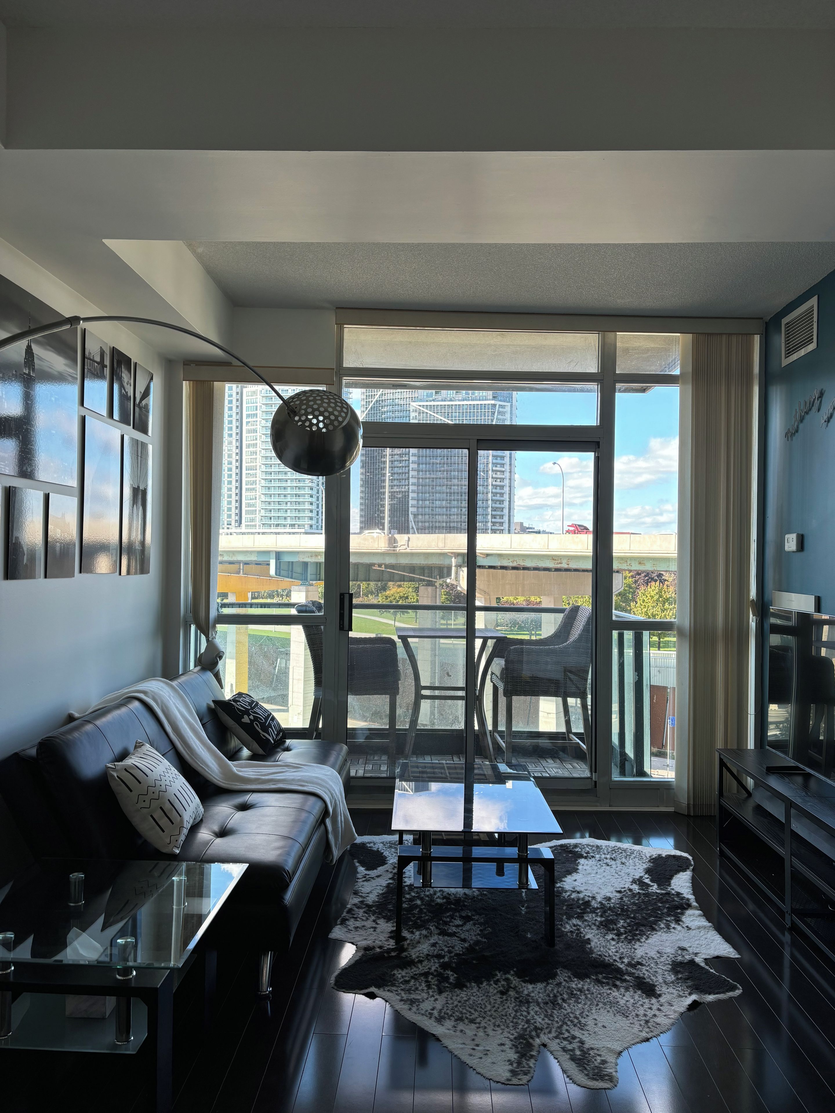 Ein modernes Wohnzimmer mit einer Ledersofa, einem Glastisch und Blick auf eine Stadtkulisse durch große Fenster.