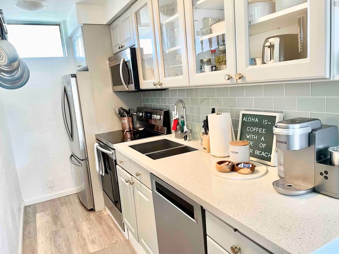 A modern kitchen with stainless steel appliances, a coffee maker, and a sign that reads 'ALOHA IS COFFEE WITH A DEE OF BEACH.'