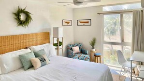 A hotel room with a bed, a ceiling fan, a window with curtains, a chair, and a small table. - Sugar Beach Shangri-La: Wake Up to the Ocean! (Kihei)
