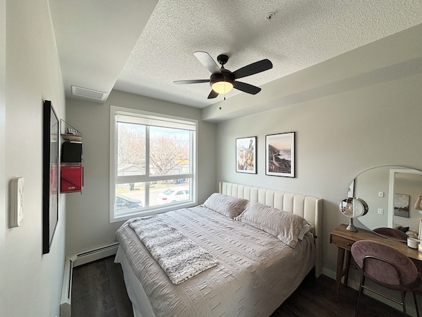 Une chambre à coucher comprenant un lit, un bureau, une chaise, un ventilateur de plafond et une fenêtre donnant sur l’extérieur.