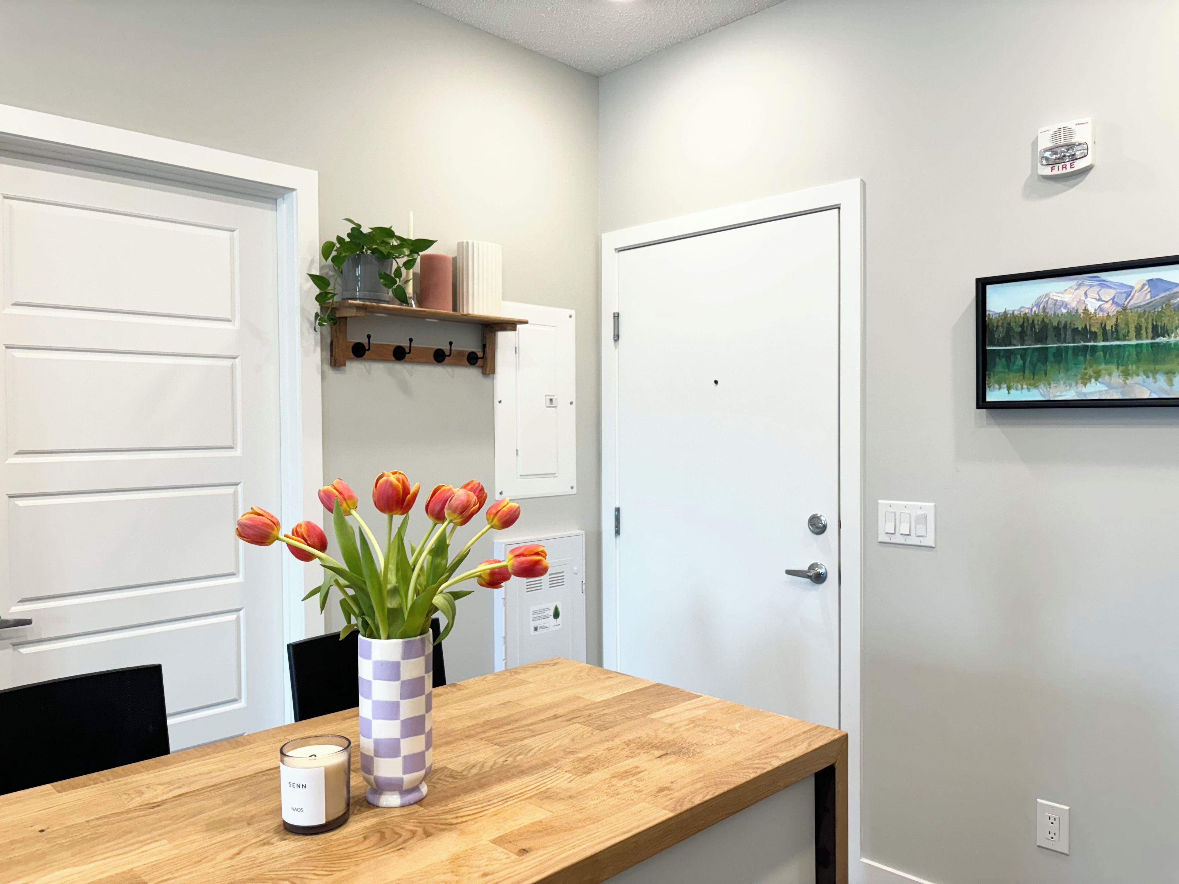 A room with a wooden table, a vase with tulips, a candle, and a framed picture on the wall.