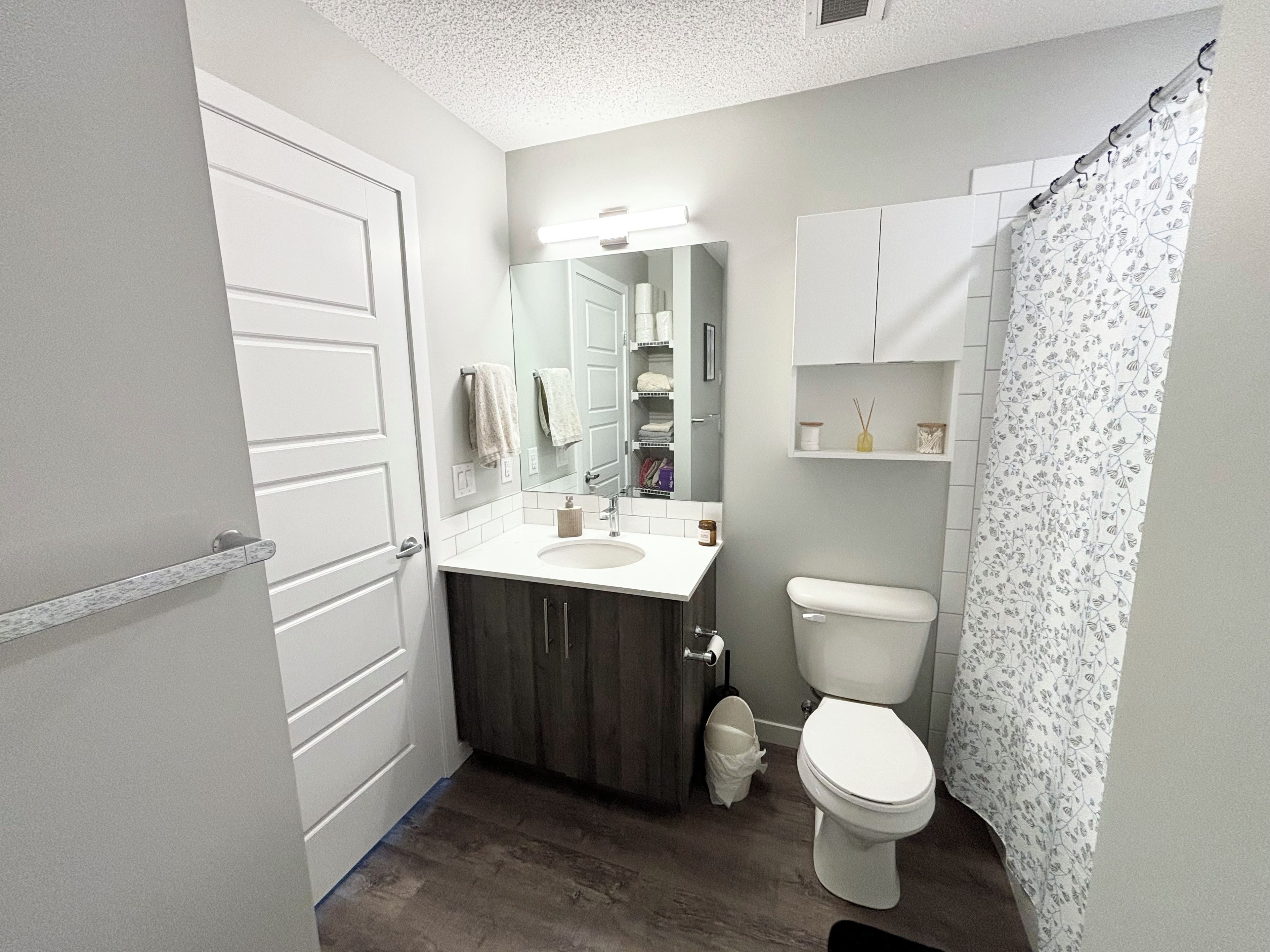 A bathroom with a white sink, dark wooden vanity, a white toilet, and a shower curtain with a floral pattern.