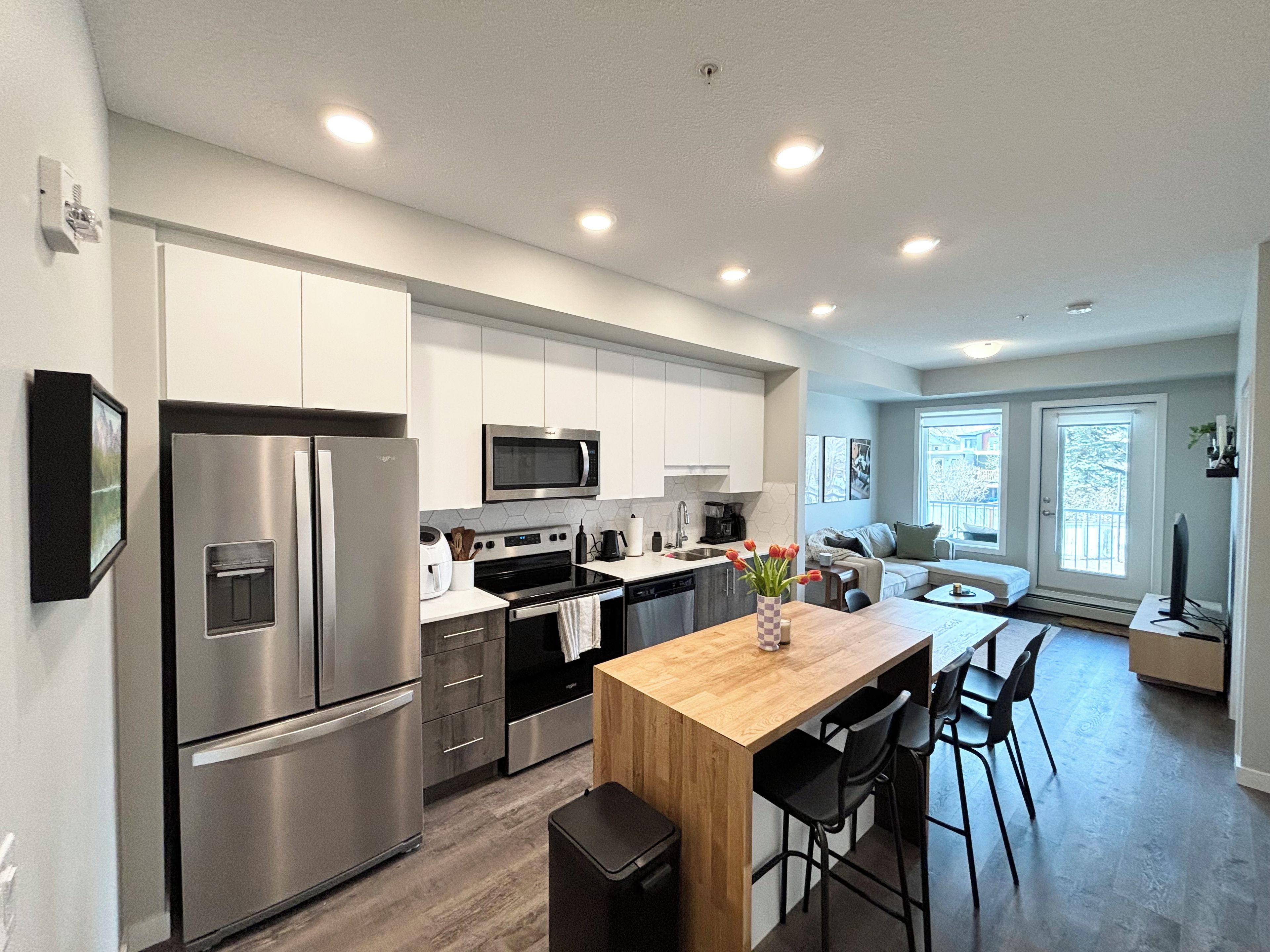 A modern kitchen with stainless steel appliances, a wooden island with bar stools, and a view to a balcony.