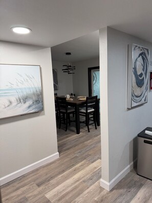 A dining area with a wooden table and chairs, a ceiling light, and a painting on the wall.