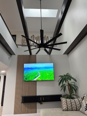 A modern living room with a flat-screen TV mounted on a wall, a ceiling fan, and a potted plant. - Ivory House Spacious 2-Story Retreat with 3 Bedrooms & Private Balcony (Lakeland)
