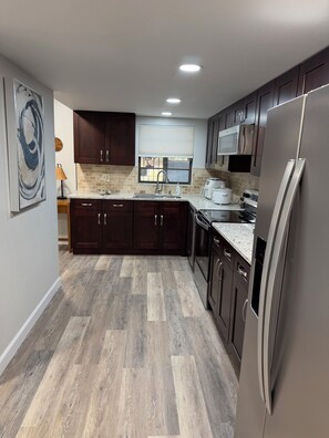 A modern kitchen with dark wooden cabinets, a stainless steel refrigerator, and a herringbone-patterned floor.