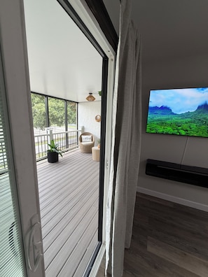 A room with a sliding glass door leading to a balcony with a wooden deck, outdoor furniture, and a television mounted on the wall. - Ivory House Spacious 2-Story Retreat with 3 Bedrooms & Private Balcony (Lakeland)
