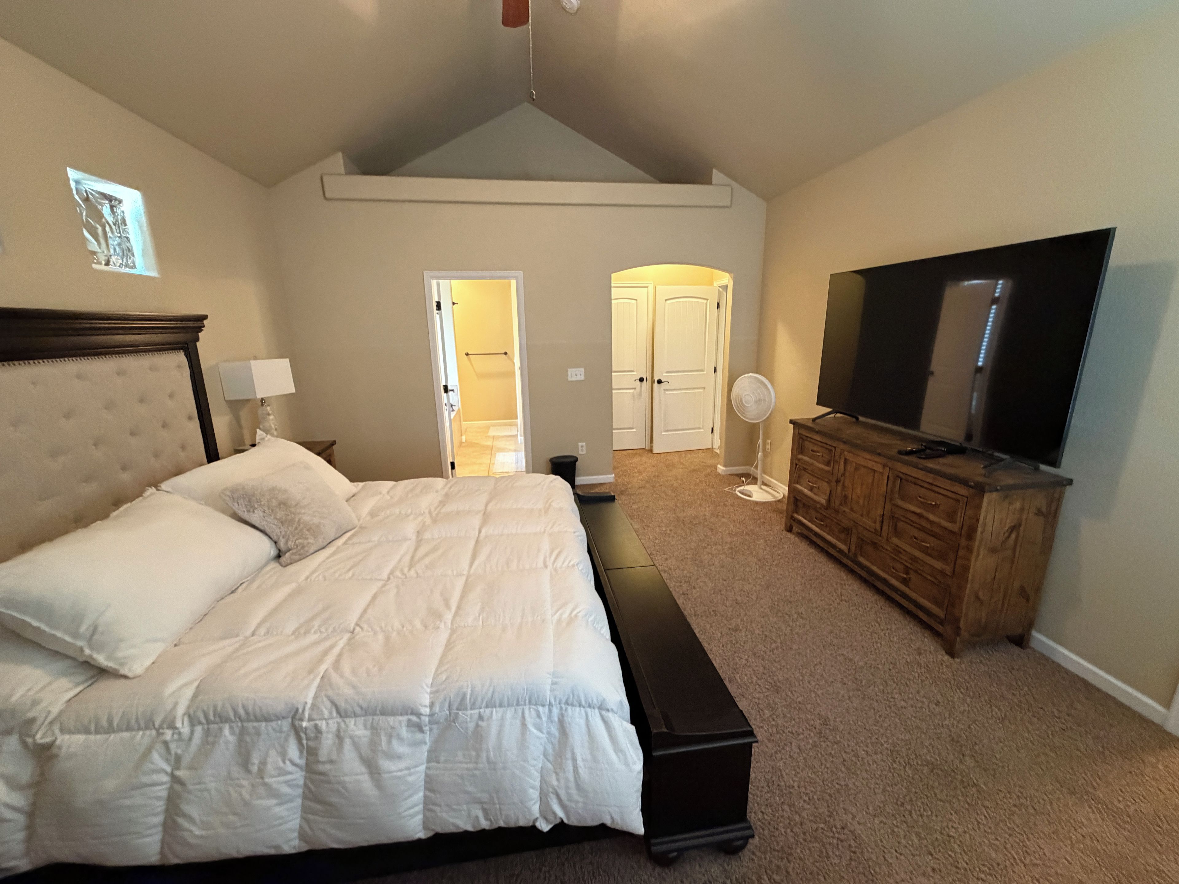 A bedroom with a bed, a dresser, a television, and a fan.