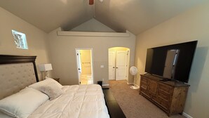 A bedroom with a bed, a dresser, a television, and a fan.