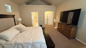 A bedroom with a bed, a dresser, a television, and a fan.