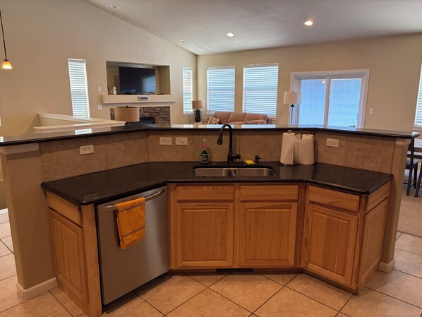 A kitchen with a built-in dishwasher, a sink, wooden cabinets, and a television above the counter.