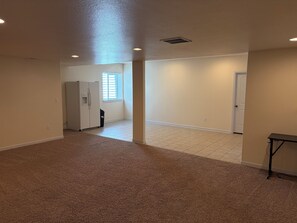A spacious room with a carpeted floor, a white refrigerator, and a door leading to another room.