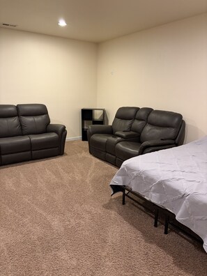A room with two leather sofas, a bed, a small black table, and a carpeted floor.