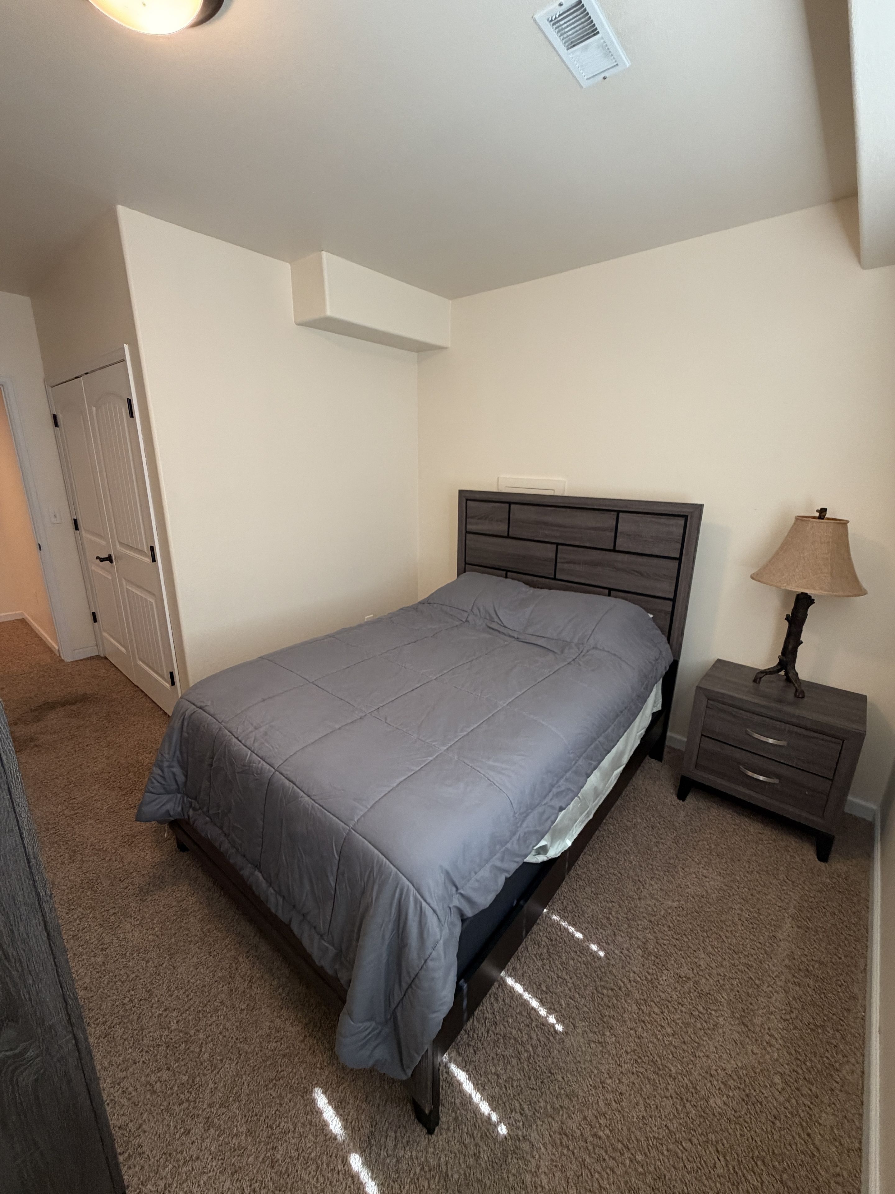 A bedroom with a bed, a nightstand, a lamp, and a door.
