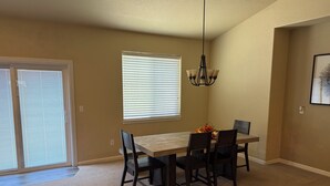 A dining area with a table and chairs, a chandelier, and a window with blinds.