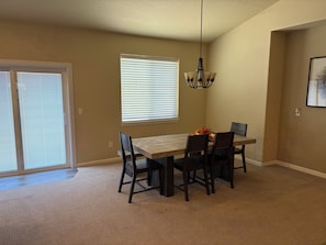 A dining area with a table and chairs, a chandelier, and a window with blinds.