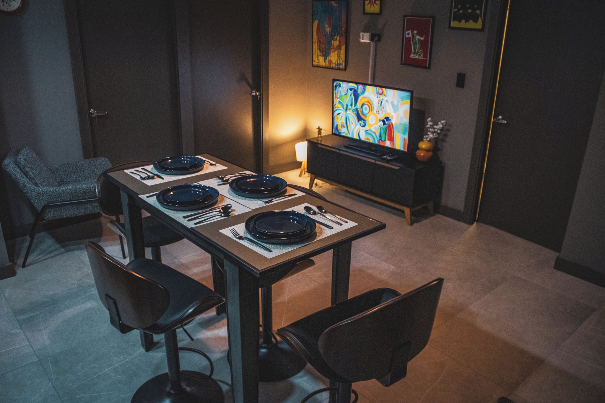 Un coin repas avec une table dressée pour quatre personnes, des chaises, un téléviseur et des œuvres d’art accrochées au mur.