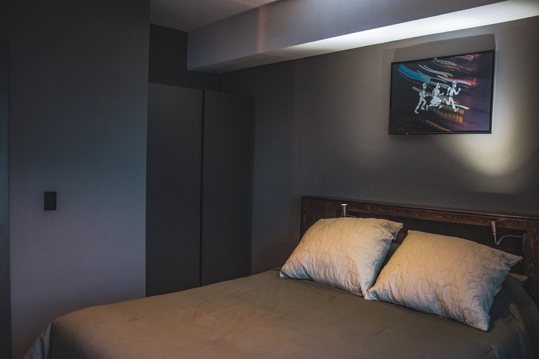 A bedroom with a bed, two pillows, a headboard, and a wall-mounted artwork.