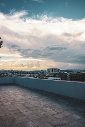 A rooftop terrace with a view of a cityscape and clouds.