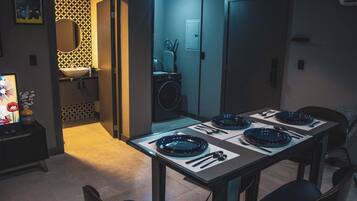 Un comedor con una mesa dispuesta para cuatro personas, una lavadora y un baño visible a través de una puerta abierta.