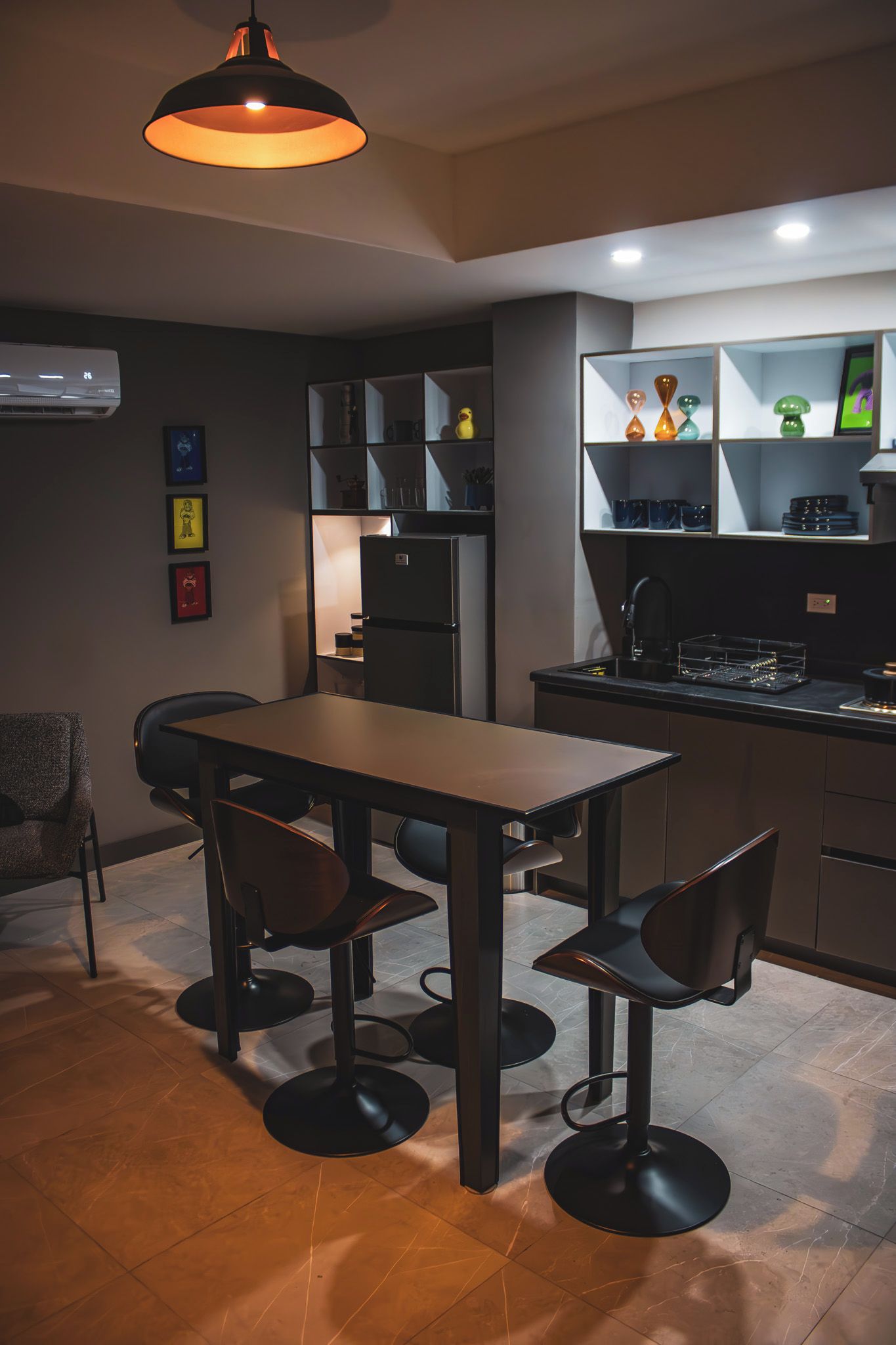 Una cucina moderna con zona pranzo, comprensiva di tavolo e sedie, un frigorifero e uno scaffale con oggetti decorativi.