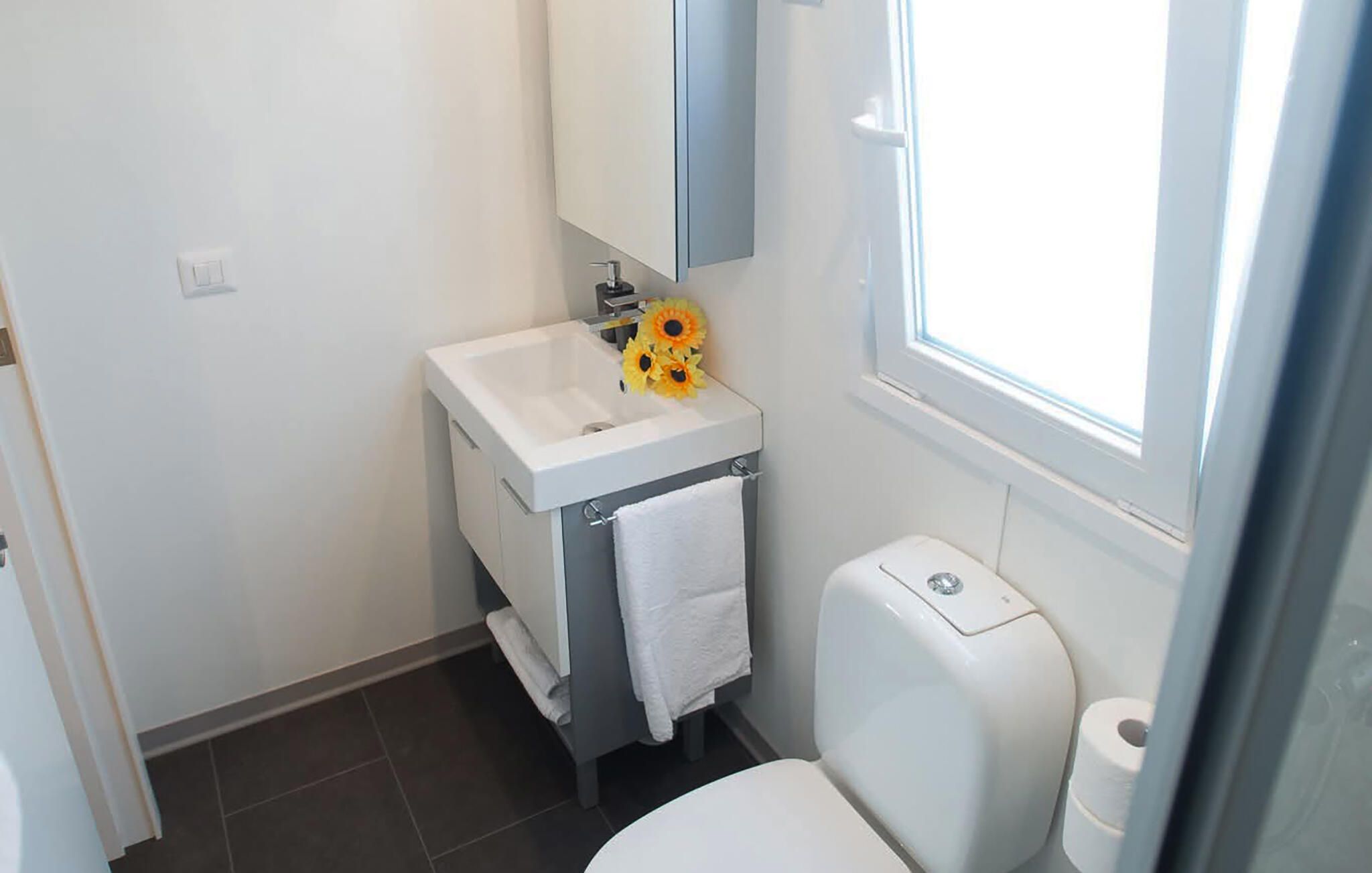 Ein kleines Badezimmer mit einem weißen Waschbecken, einem Spiegel, einer Toilette und einem Fenster.