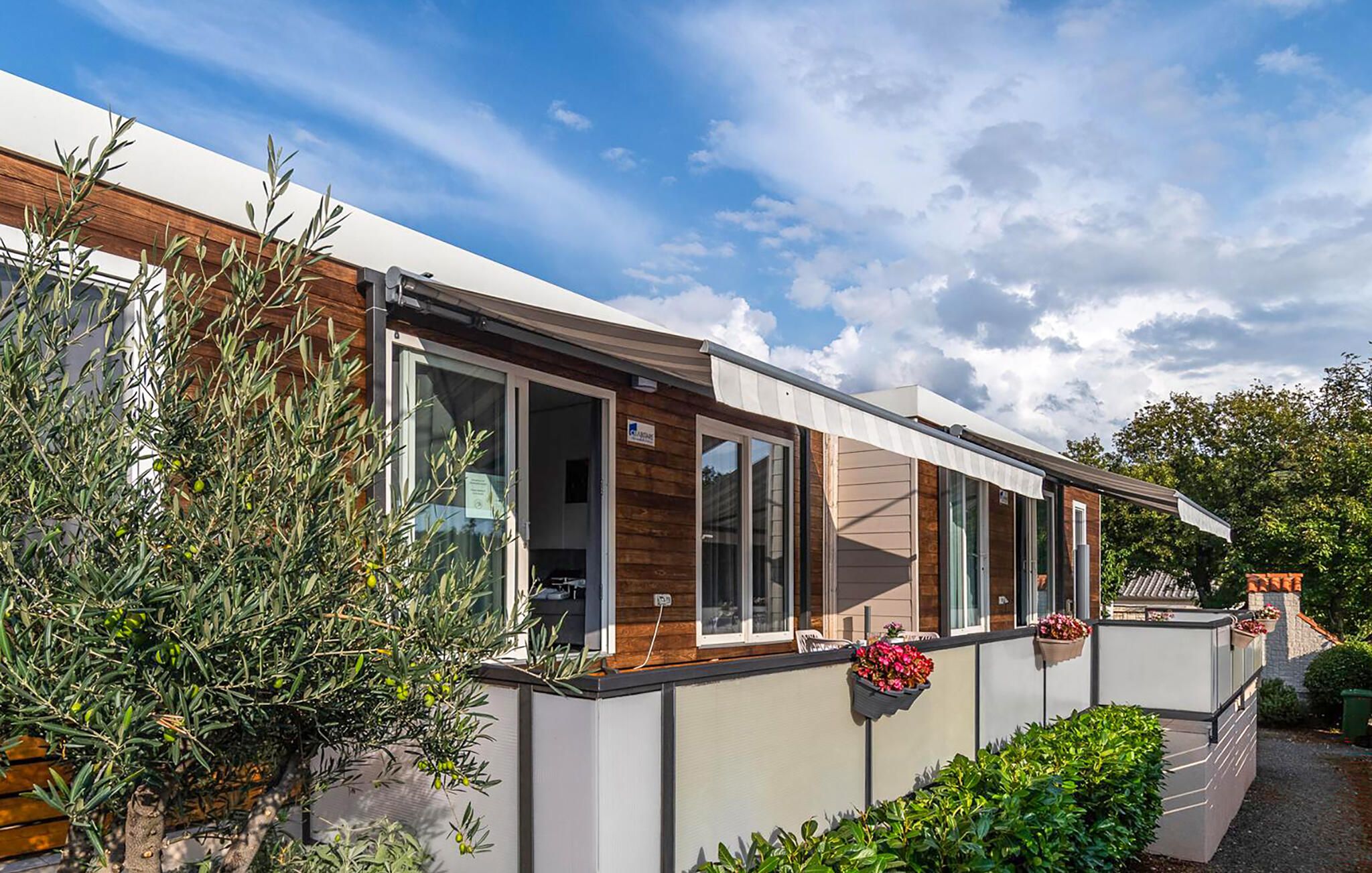 Une maison mobile moderne dotée de grandes fenêtres, d’un revêtement extérieur en bois et d’un jardin bien entretenu.