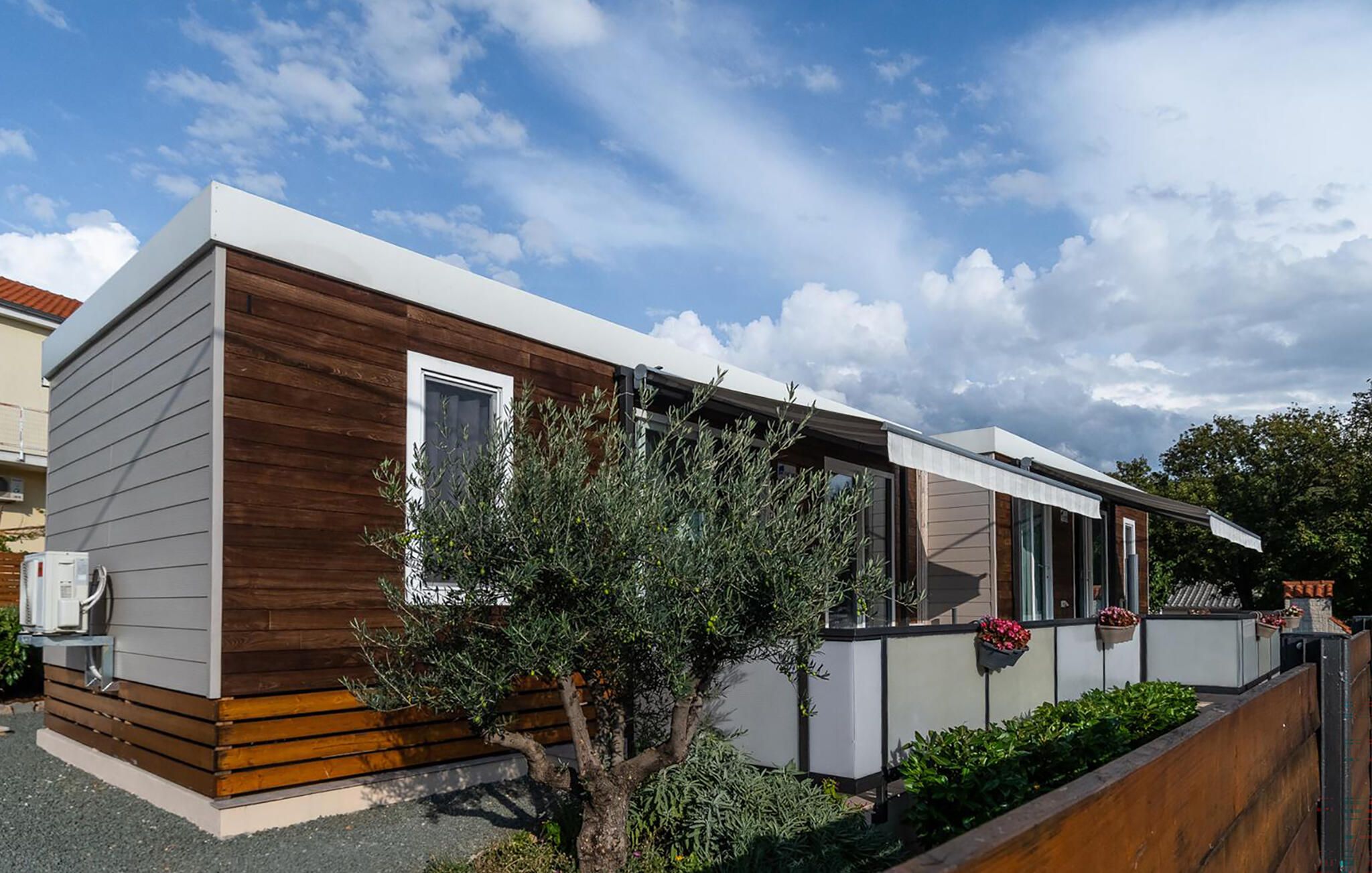 Uma casa moderna térrea com fachada de madeira, janelas amplas e um pequeno jardim.