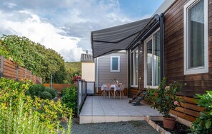 Eine Terrassenfläche mit Tisch und Stühlen, ein Holzzaun und ein Garten mit verschiedenen Pflanzen.