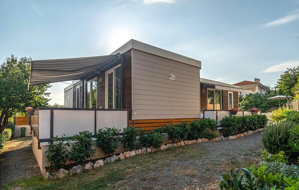 Ein modernes Einfamilienhaus mit überdachter Veranda, einer Steinmauer und einem gepflegten Garten.
