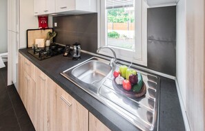 Eine Küche mit einer Spüle aus Edelstahl, Holzschränken und einem Fenster mit Jalousien.