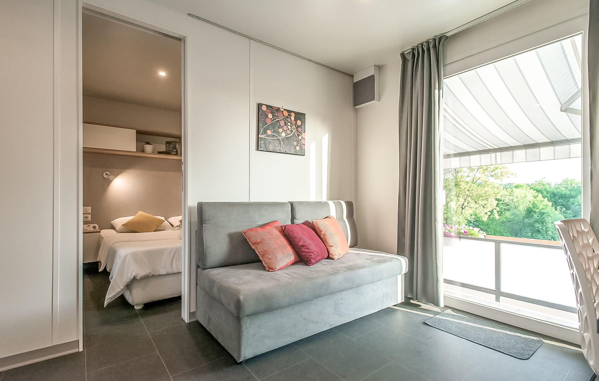 A modern bedroom with a grey sofa, a bed, and a large window with curtains.