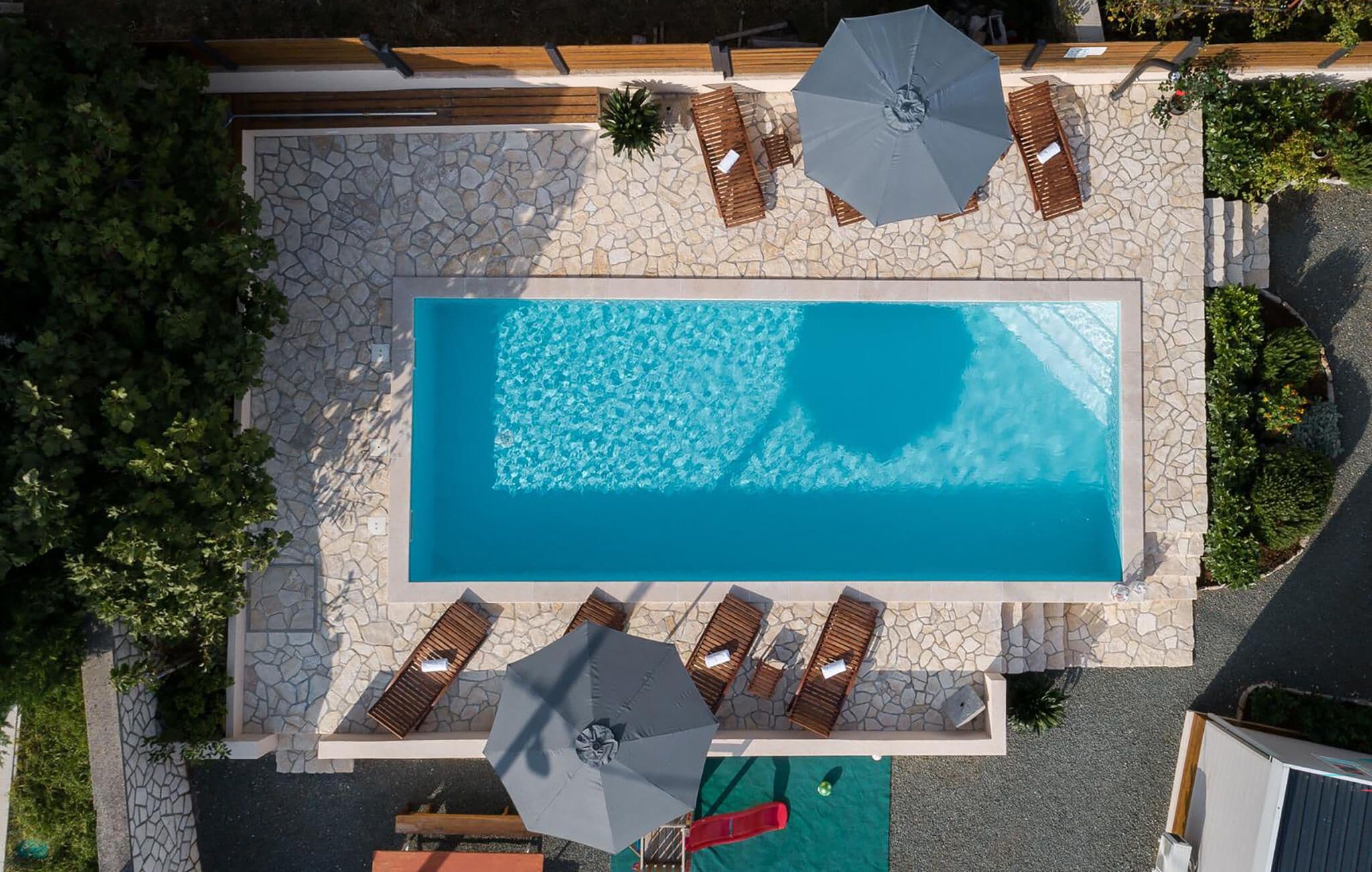 Piscina retangular com borda de pedra, rodeada por espreguiçadeiras e guarda-sóis.