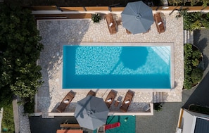 Ein rechteckiger Swimmingpool mit Steinrand, umgeben von Liegestühlen und Sonnenschirmen.