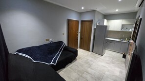 A compact room with a bed, a kitchenette, and a door leading to another room. - Velvet Suite | Modern 1-Bedroom Budget Retreat- Central calm location (Accra)