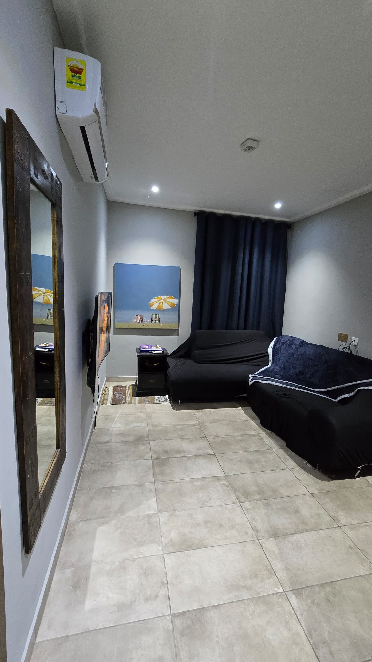 Une pièce comprenant un lit, une petite table, une chaise, un tableau représentant une scène de plage et un miroir.