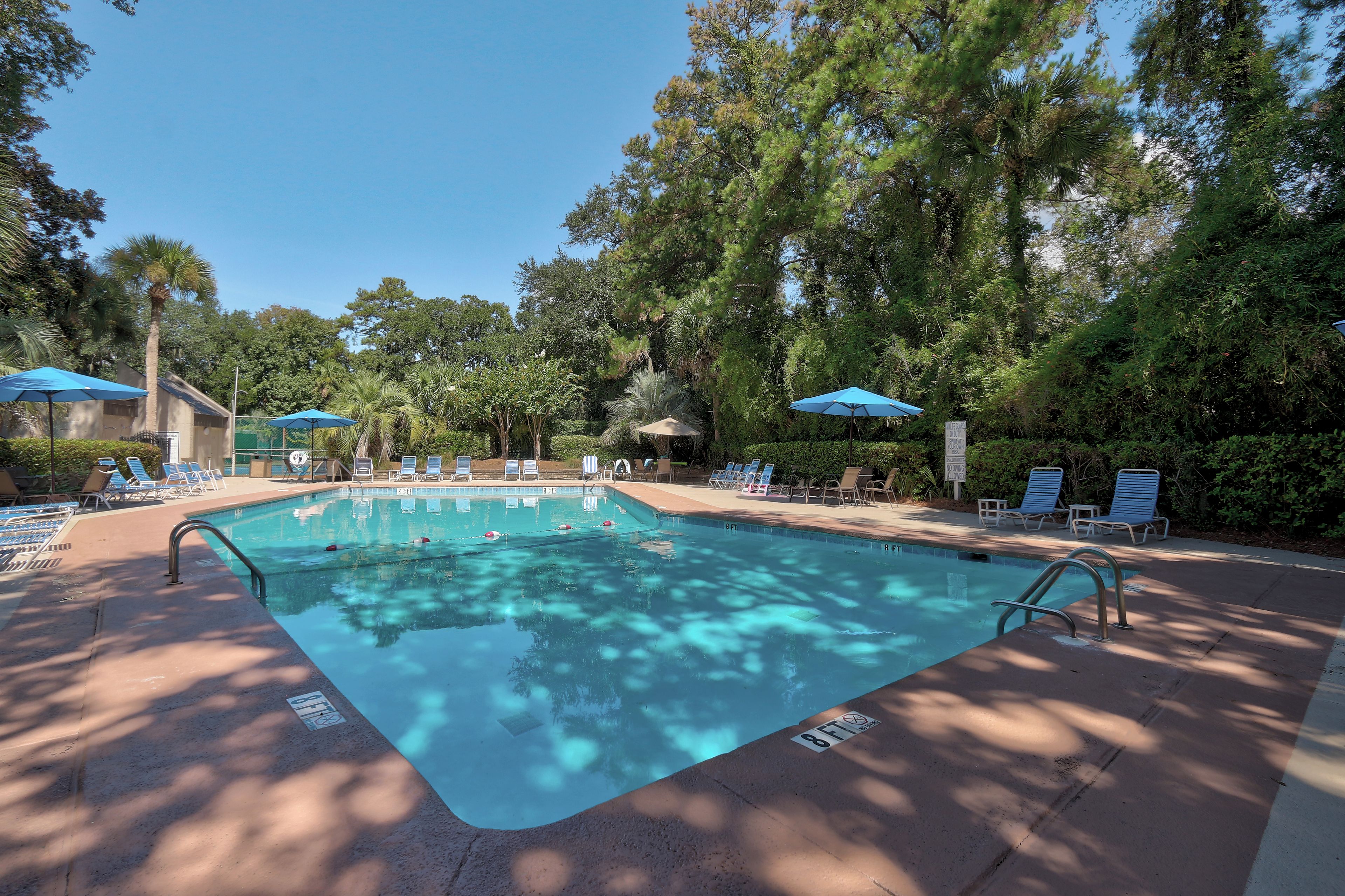 A swimming pool with lounge chairs and umbrellas, surrounded by trees.