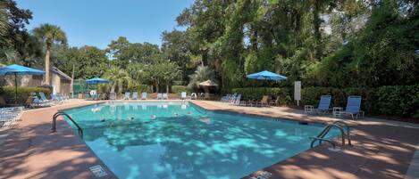 A swimming pool with lounge chairs and umbrellas, surrounded by trees.