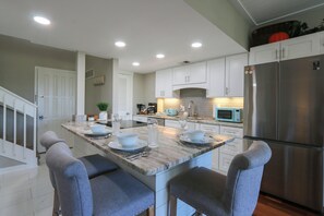 A modern kitchen with white cabinets, a stainless steel refrigerator, and a marble island with bar stools. - Walk to Beach & Coligny/King Bed/Pickleball/Pool (Hilton Head Island)
