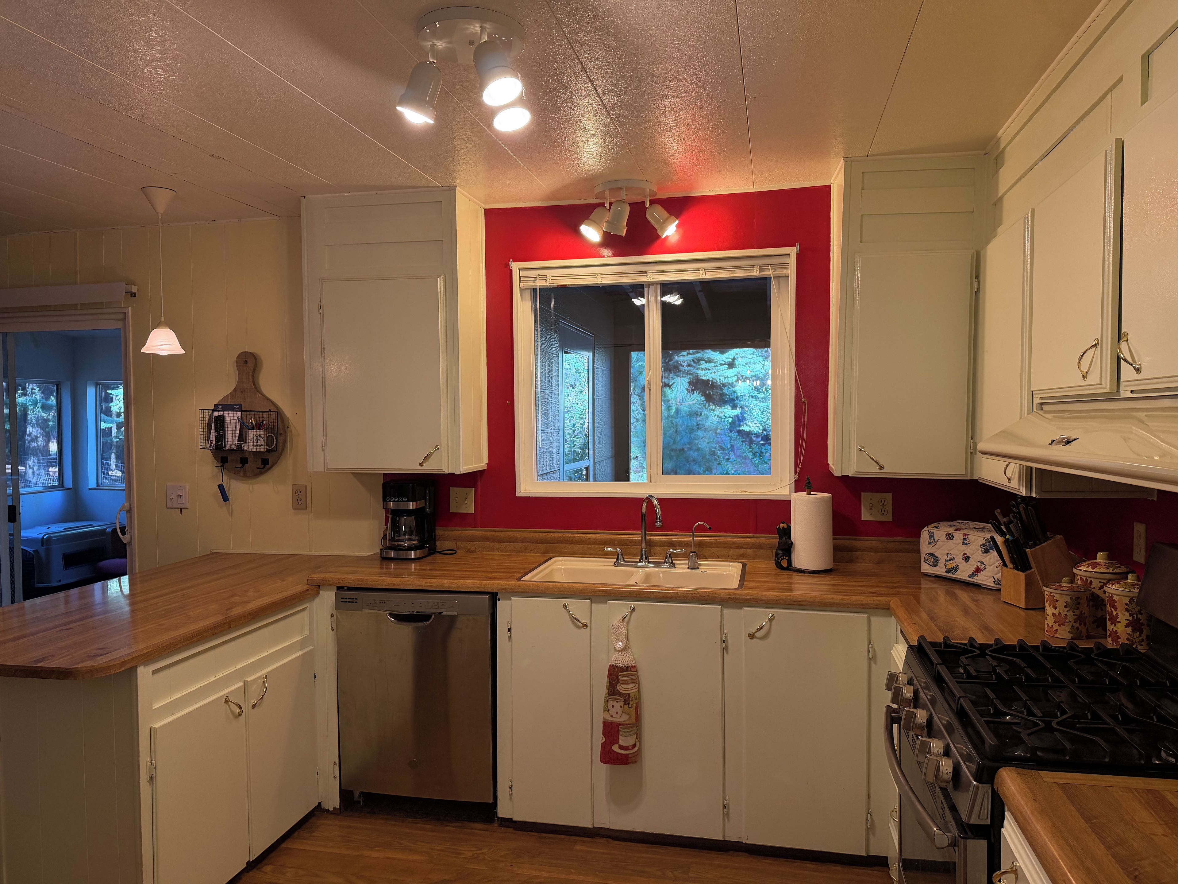 A kitchen with white cabinets, a dishwasher, a stove, and a window with a view of greenery.