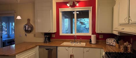A kitchen with white cabinets, a dishwasher, a stove, and a window with a view of greenery.