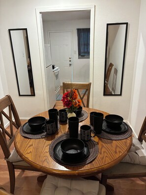 A dining table with black tableware and a vase of flowers, surrounded by chairs and mirrors on the walls.